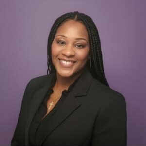Professional woman smiling in black blazer against purple background.